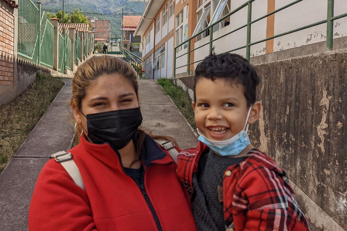 Bimbo peruviano guarda di lato mentre viene tenuto in braccio dalla madre che guarda dritto verso la fotocamera. Entrambi indossano una maglietta o giacca rossa